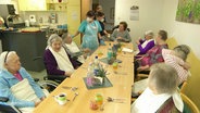 Eine Pflegekraft singt mit mehreren Senioren in einem Heim. © Screenshot 