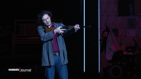 Ein Mann mit einem Gewehr auf der Bühne. © Screenshot 