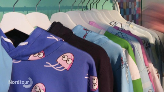 Bunte Pullover mit Motiven hängen auf Kleiderbügeln. © Screenshot 