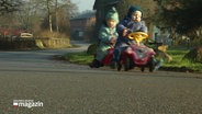 Zwei Kleinkinder fahren mit ihren Bobby-Cars über die Jahrsdorfer Straßen. © Screenshot 