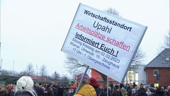 Bei einer Demonstration wird ein größeres Schild mit Forderungen aus der Menge empor gehalten. © Screenshot 