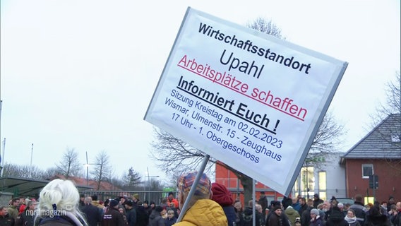 Bei einer Demonstration wird ein größeres Schild mit Forderungen aus der Menge empor gehalten. © Screenshot 