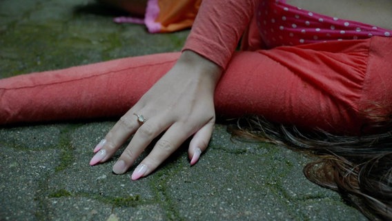 Eine Frau liegt auf dem Boden, an ihrer Hand fehlt einer der künstlichen Fingernägel. © Screenshot 