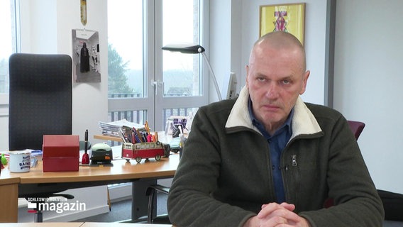 Rainer Jürgensen, grimmig guckend, an einem Tisch sitzend © Screenshot 