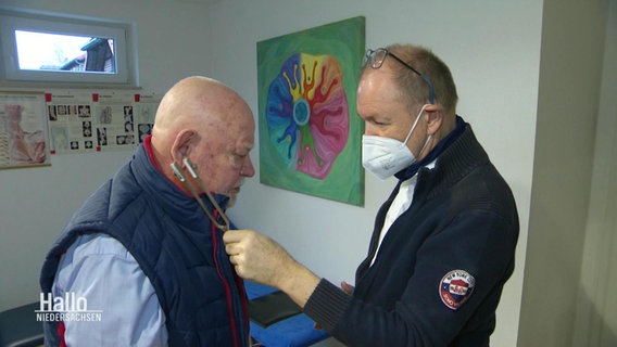 Ein Arzt hält einem älteren Patienten eine Stimmgabel ans Ohr. © Screenshot 