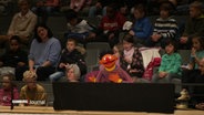 Sesamstraßen-Figur "Ernie" sing ein Lied in der Elbphilharmonie. Hinter ihm sitzen Kinder im Publikum. © Screenshot 