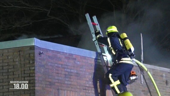 Eine Einsatzkraft der Feuerwehr steigt eine Leiter empor um bei Nacht auf ein Flachdach eines Gebäudes zu gelangen. © Screenshot 