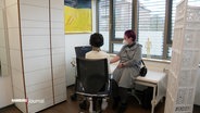 In einer Rheumatologischen Praxis sitzt eine Patientin auf einer Behandlungsliege während eine Ärztin ihr Handgelenk sonographisch untersucht. © Screenshot 