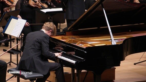 Pianist Jan Liesiecki spielt am Flügel auf der Bühne vor dem Royal Philharmonic Orchestra im großen Saal der Elbphilharmonie. © Screenshot 