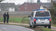 Am Rand einer Landstraße ist ein Einsatzfahrzeug der Polizei geparkt, daneben stehen zwei Beamte. © Screenshot 