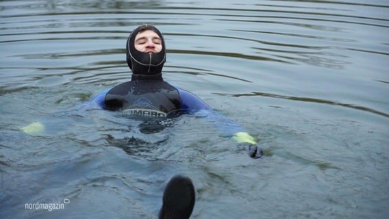 Ein junger Mann im Taucheranzug in einem See. © Screenshot 