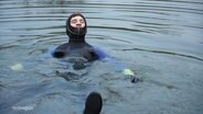Ein junger Mann im Taucheranzug in einem See. © Screenshot 