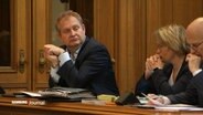 Hamburger Umweltsenator Kerstan sitzt in einem Plenarsaal neben Herrn Tschentscher und einer weiteren Kollegin. © Screenshot 