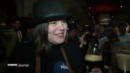 Katharine Fegebank im Interview, sie trägt einen schwarzen Hut und hält ein Bier in der Hand. © Screenshot 