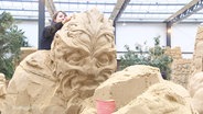 Eine Carverin fertigt eine Sandskulptur für die Ausstellung in Prora auf Rügen an. © Screenshot 