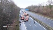Einsatzkräfte der Feuerwehr sichern eine Unfallstelle auf der Autobahn ab. DAhinter staut sich eine lange Autoschlange. © Screenshot 