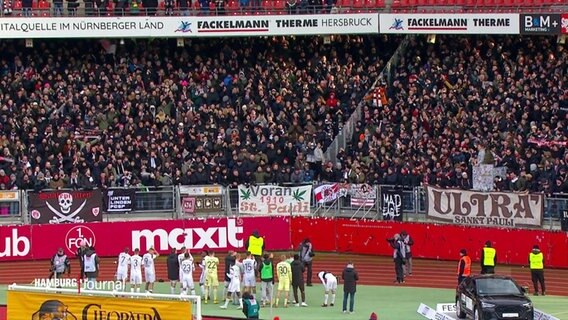 In einer Stadionkurve feiern sich Fans von FC St. Pauli und die Spieler auf dem Feld für einen Sieg. © Screenshot 