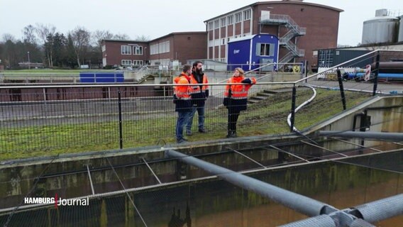 Drei Personen in orange-farbener Arbeitskleidung stehen an einem Wiederaufbereitungsbecken auf dem Gelände eines Wasserwerks. © Screenshot 