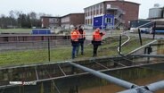 Drei Personen in orange-farbener Arbeitskleidung stehen an einem Wiederaufbereitungsbecken auf dem Gelände eines Wasserwerks. © Screenshot 