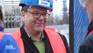 Christian Meyer, Niedersachsens Umwelt- und Energieminister von den Grünen, trägt bei einer Werksbegehung eine rote Warnweste und einen blauen Helm mit der Aufschrift "RWE". © Screenshot 
