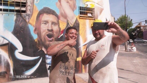 Zwei argentinische Fußballfans machen ein Selfie vor einem Messi-Mural. © Screenshot 