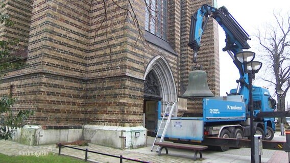 Eine Glocke hängt an einem Kran vor einer Kirche. © Screenshot 