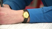 Nahaufnahme einer schriebenden person, die eine Armbanduhr trägt. © Screenshot 