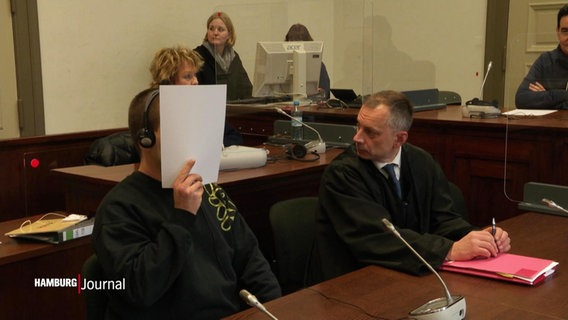 Der Verurteilte mit einem Stapel Papier vor dem Gesicht und seinem Anwalt neben sich. © Screenshot 