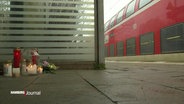 Eine kleine Gedenkstätte mit Kerzen und Blumen auf dem Gelis eines Bahnhofes © Screenshot 