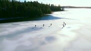 Sechs schlittschufahrende Menschen aus der Vogelperspektive. © Screenshot 