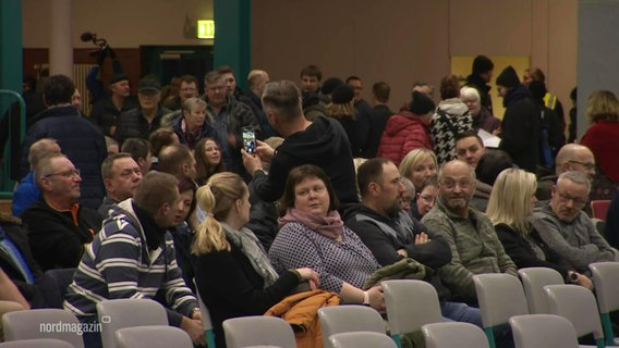 Bei einer Bürgerversammlung sitzen viele Menschen in Stuhlreihen in einer Turnhalle. © Screenshot 