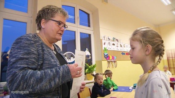 Eine Lehrerin überreicht einer Grundschülerin ihr Zeugnis vor der Klasse. © Screenshot 