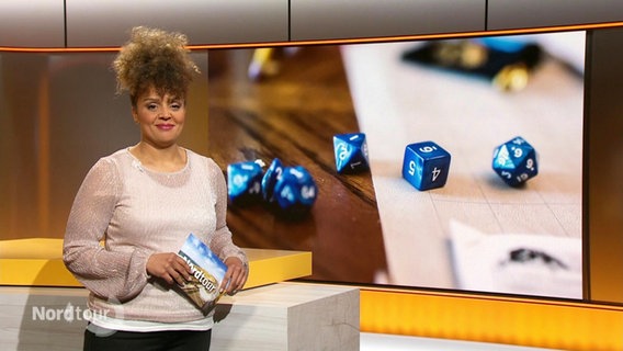 Die Moderatorin Nadja Babalola, im Hintergrund ein Bild mit blauen Würfeln. © Screenshot 