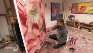 Ein junger Mann arbeitet in einem Artelier an einem großen Gemälde. © Screenshot 