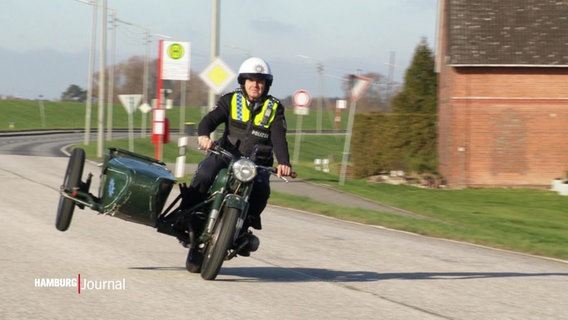 Der Polizist, der für Ochsenwerder zuständig ist, fährt auf einer Deichstrasse mit einem Motorrad mit Beiwagen © Screenshot 