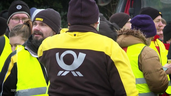 Bei einer Streikkundgebung steht ein Mann mit einer gelben Jacke der deutschen Post mit dem Rücken zur Kamera. © Screenshot 