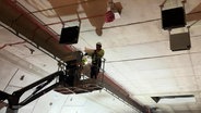 Zwei Arbeiter arbeiten von dem Korb eines Hubkrans aus an der Decke eines neugebauten Tunnels. © Screenshot 