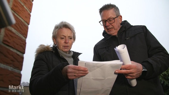 Ein Mann und eine Frau gucken verwirrt auf einen größeres Blatt Papier. © Screenshot 