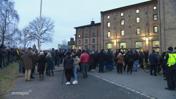 Eine Menge an Menschen vor einem Backsteingebäude © Screenshot 