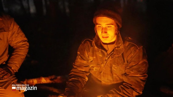 Ein junger Mann sitzt an einem Lagerfeuer. © Screenshot 