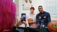 Basketballstar Chris Carter macht in einer Bücherhalle ein Foto mit einem Fan bei einer Lesung seines neuen Romans. © Screenshot 
