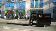 Ein Paketzusteller fährt auf einem zum Paketmobil umgerüsteten Lastenrad auf einer Straße. © Screenshot 