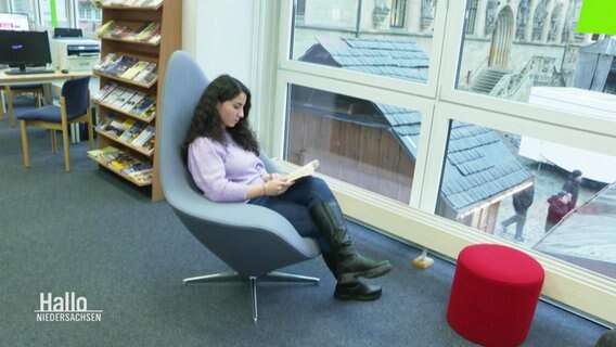 Eine Frau sitzt in einer Stadtbibliothek in einem Sessel und liest ein Buch. © Screenshot 