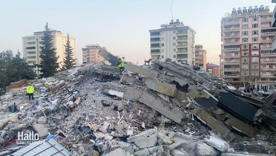 Rettungskräfte stehen auf einem Haufen Schutt nach einem Erdbeben in der Türkei. © Screenshot 