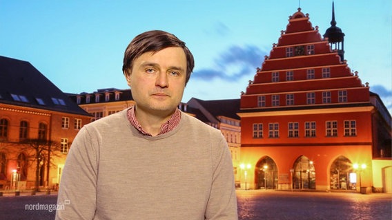 Der Ukrainistiker, Professor Roman Dubasevych, vor einer Leinwand mit dem projizierten Bild eines größeren Platzes in einer Altstadt. © Screenshot 