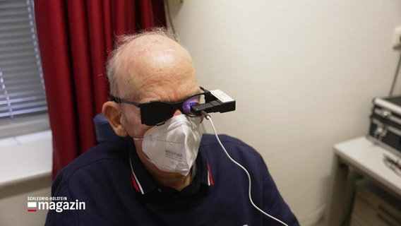 Ein älterer Mann mit FFP2-Maske schaut durch ein augenärztliches Gerät © Screenshot 
