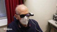 Ein älterer Mann mit FFP2-Maske schaut durch ein augenärztliches Gerät © Screenshot 