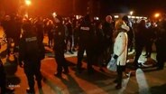 Szene einer Demonstration, Polizistinnen und Polizisten in Uniform sowie Bürgerinnen und Bürger, abends auf der Straße. © Screenshot 