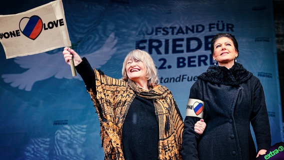 Sahra Wagenknecht und Alice Schwarzer mit einer One-Love-Fahne in russischen Farben. (extra 3 vom 02.03.2023 im Ersten) © NDR 