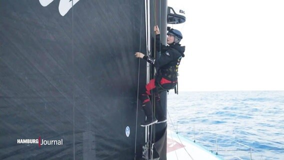Rosalin Kuiper, Crewmitglied der Malizia, steigt den Mast des Sportbootes hinauf. Sie hängt an einem Seil und trägt zur Sicherheit einen Helm. © Screenshot 